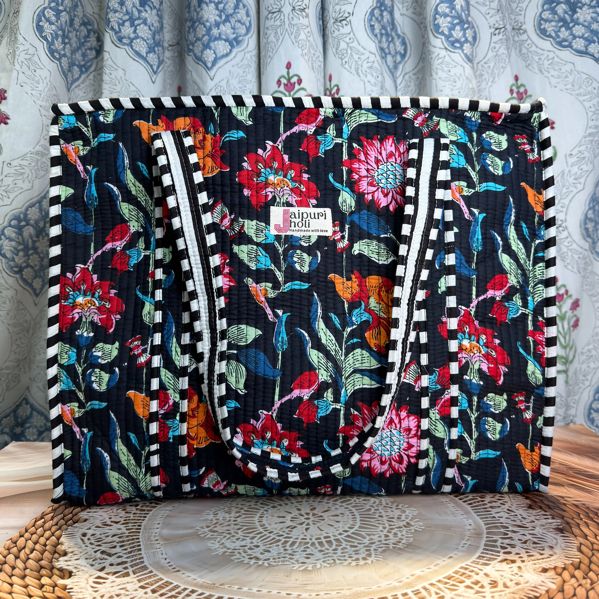 Black quilted cotton tote bag with multicolor floral hand block design, striped geometric borders, and zip closure, spacious everyday carryall.