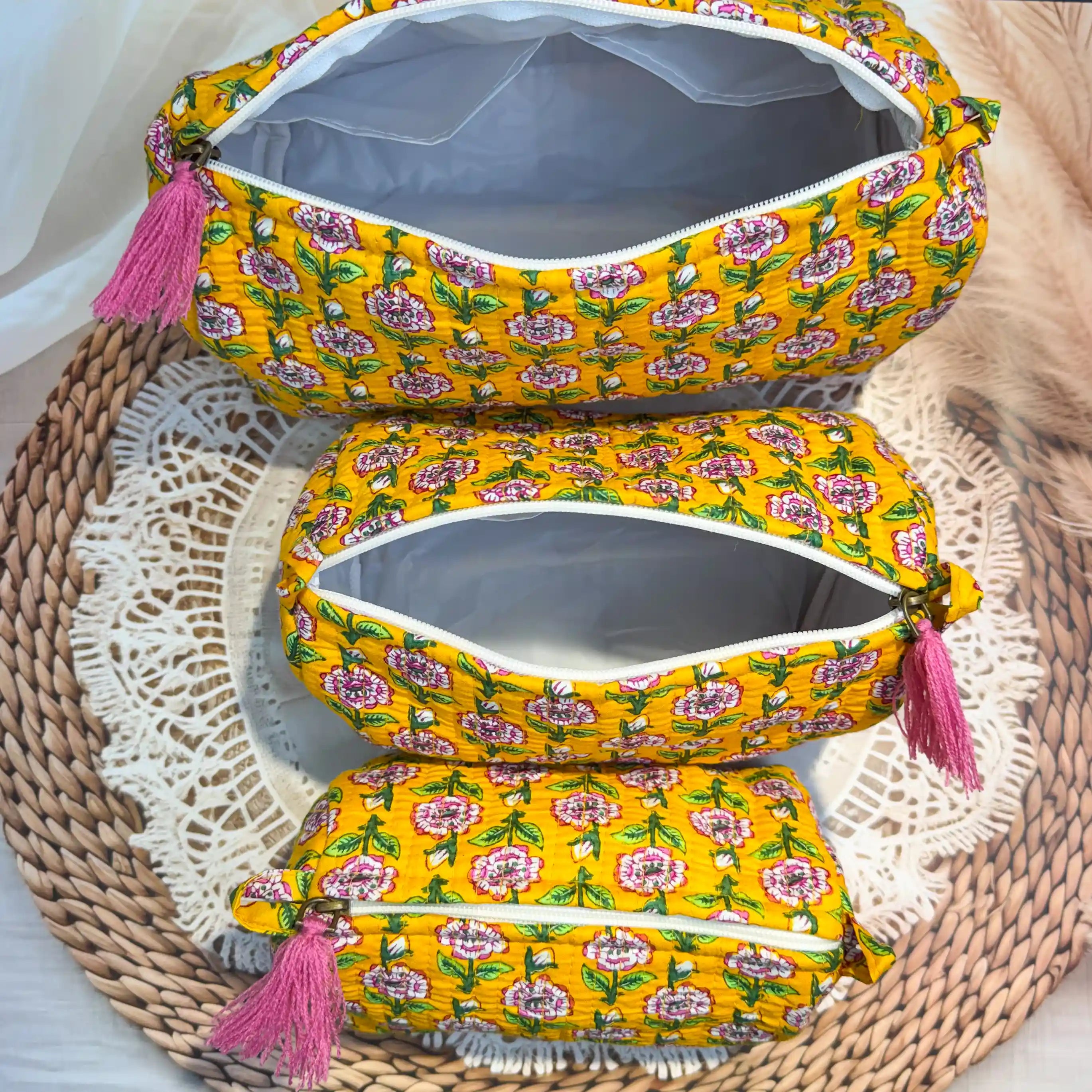 Bright yellow quilted cotton toiletry pouch set with pink and white floral hand block print pattern, three-piece organizer with pink tassels for travel essentials.