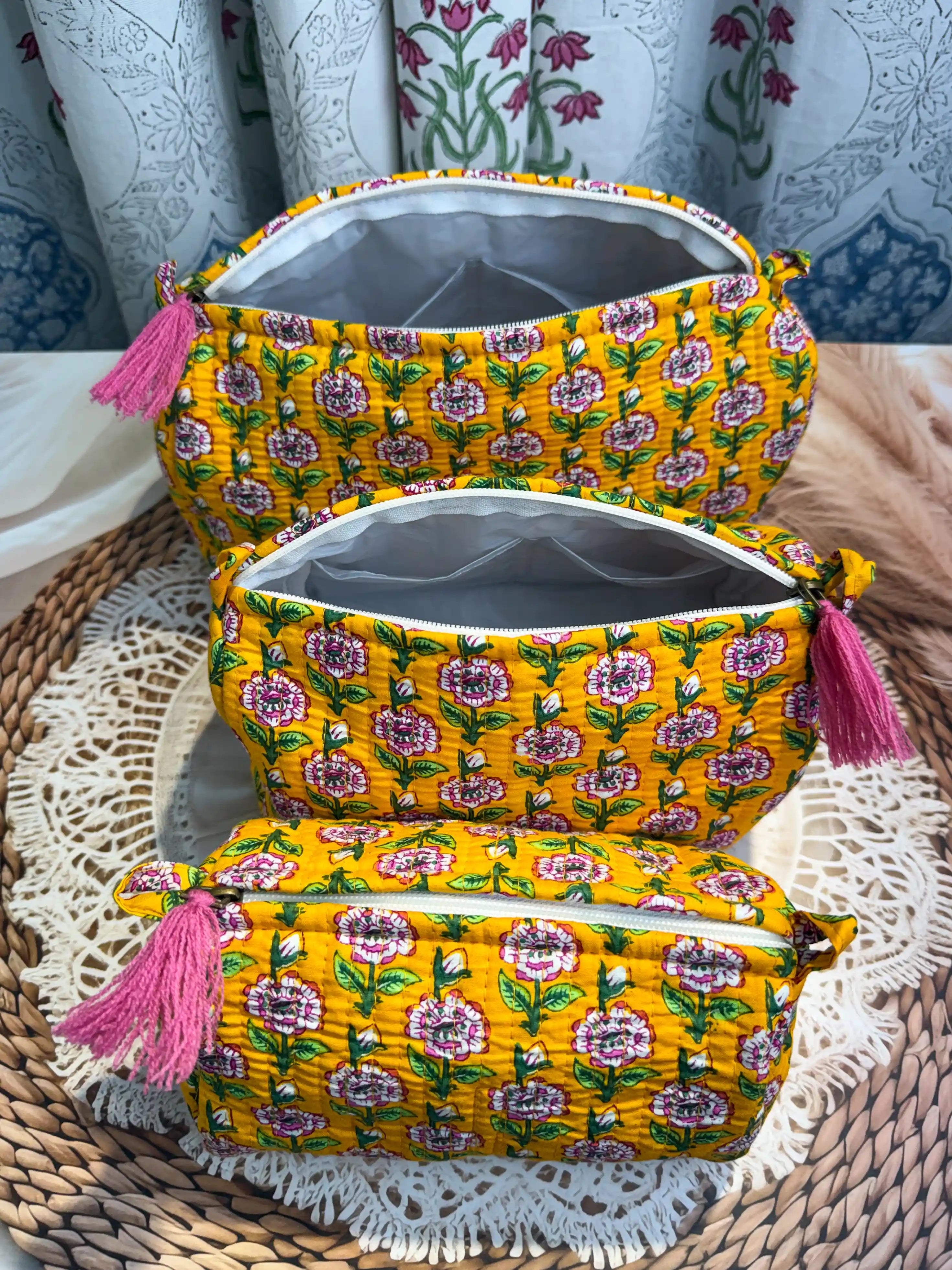 Bright yellow quilted cotton toiletry pouch set with pink and white floral hand block print pattern, three-piece organizer with pink tassels for travel essentials.