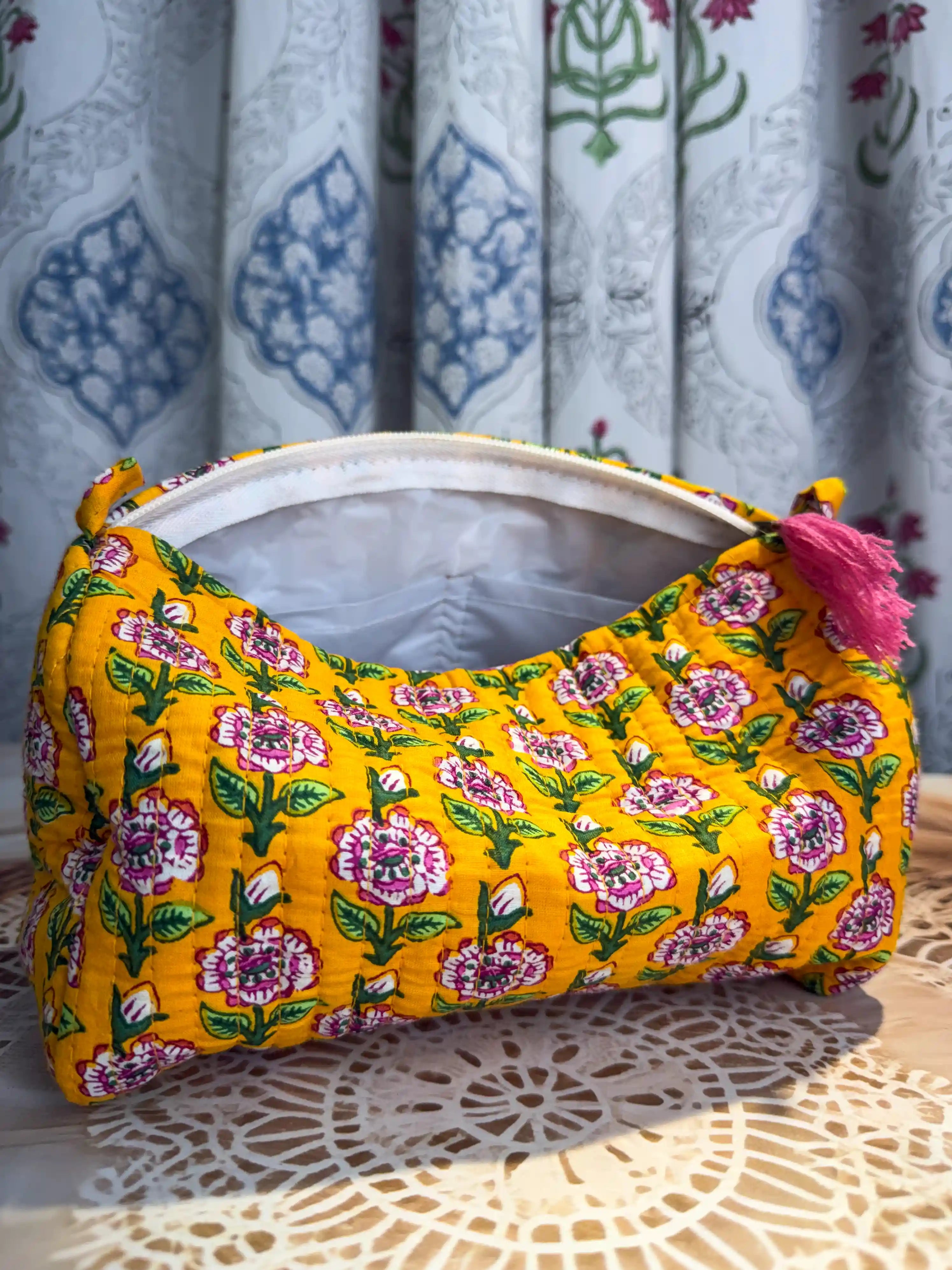 Bright yellow quilted cotton toiletry pouch set with pink and white floral hand block print pattern, three-piece organizer with pink tassels for travel essentials.
