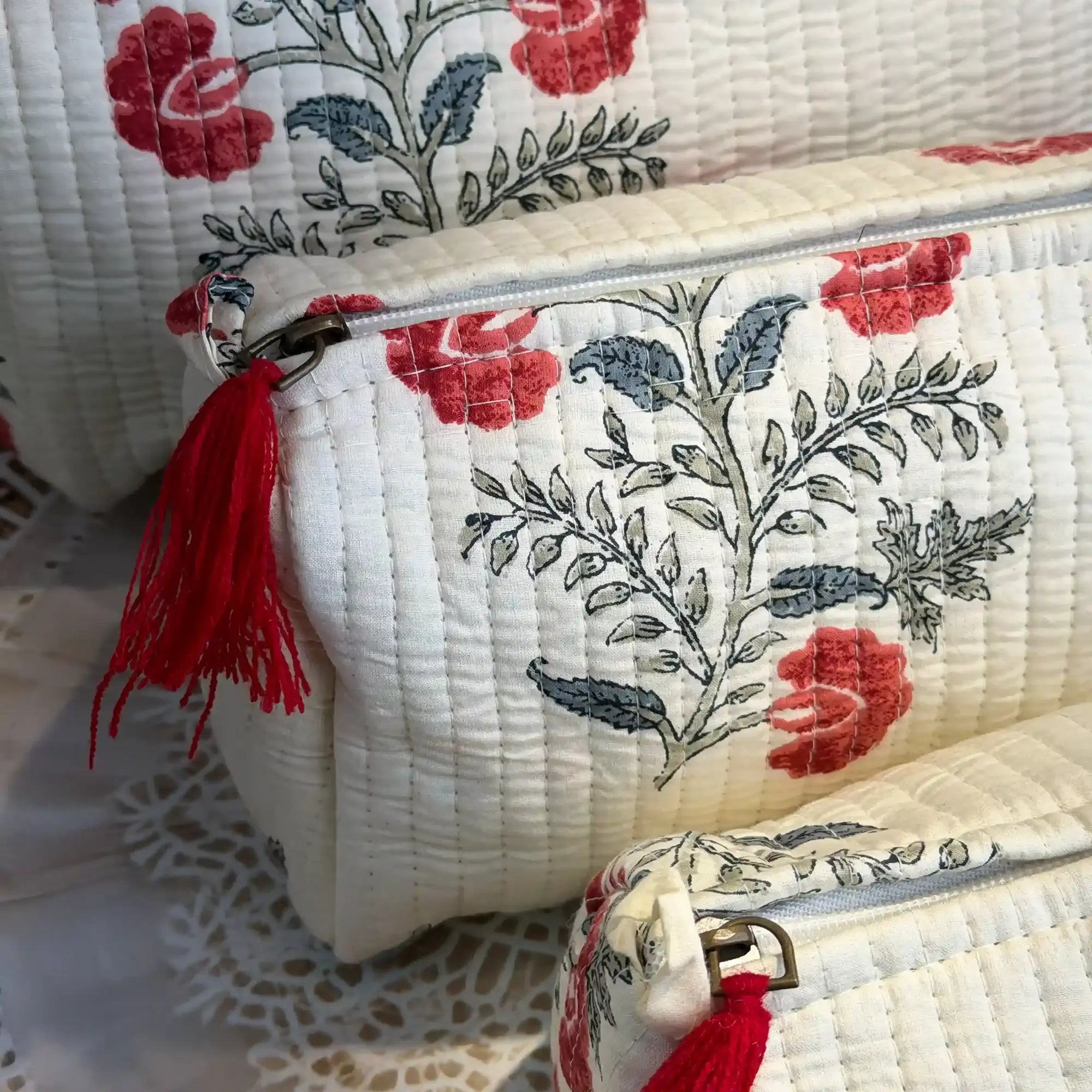 White quilted cotton toiletry pouch set with red and green botanical floral hand block print, three-piece handcrafted organizer with tassels for travel.