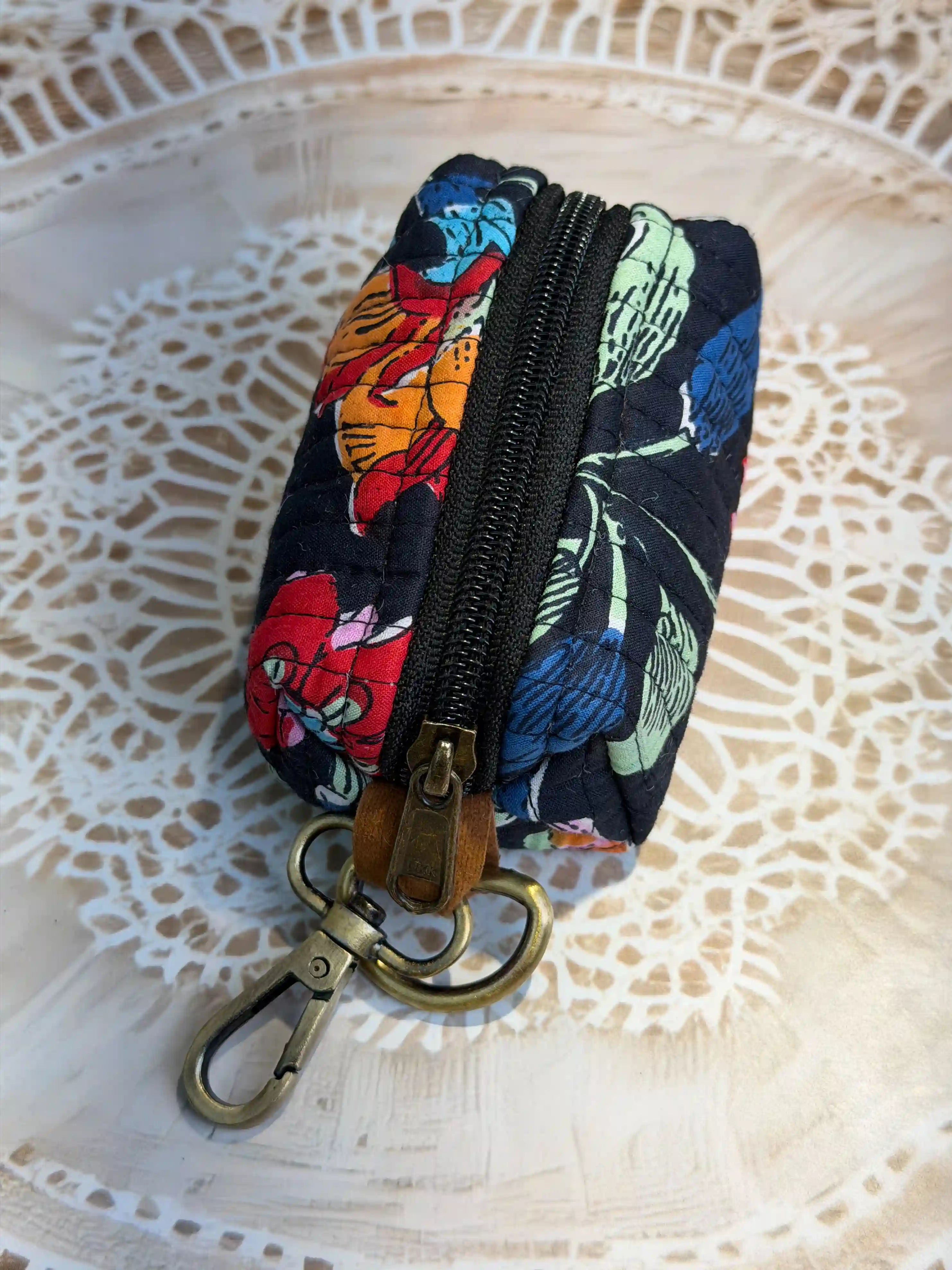 Hand block printed quilted cotton keychain pouch with multicolor floral design on black background, featuring red, yellow, and blue flowers with zip closure and metal keyring for coins and keys.