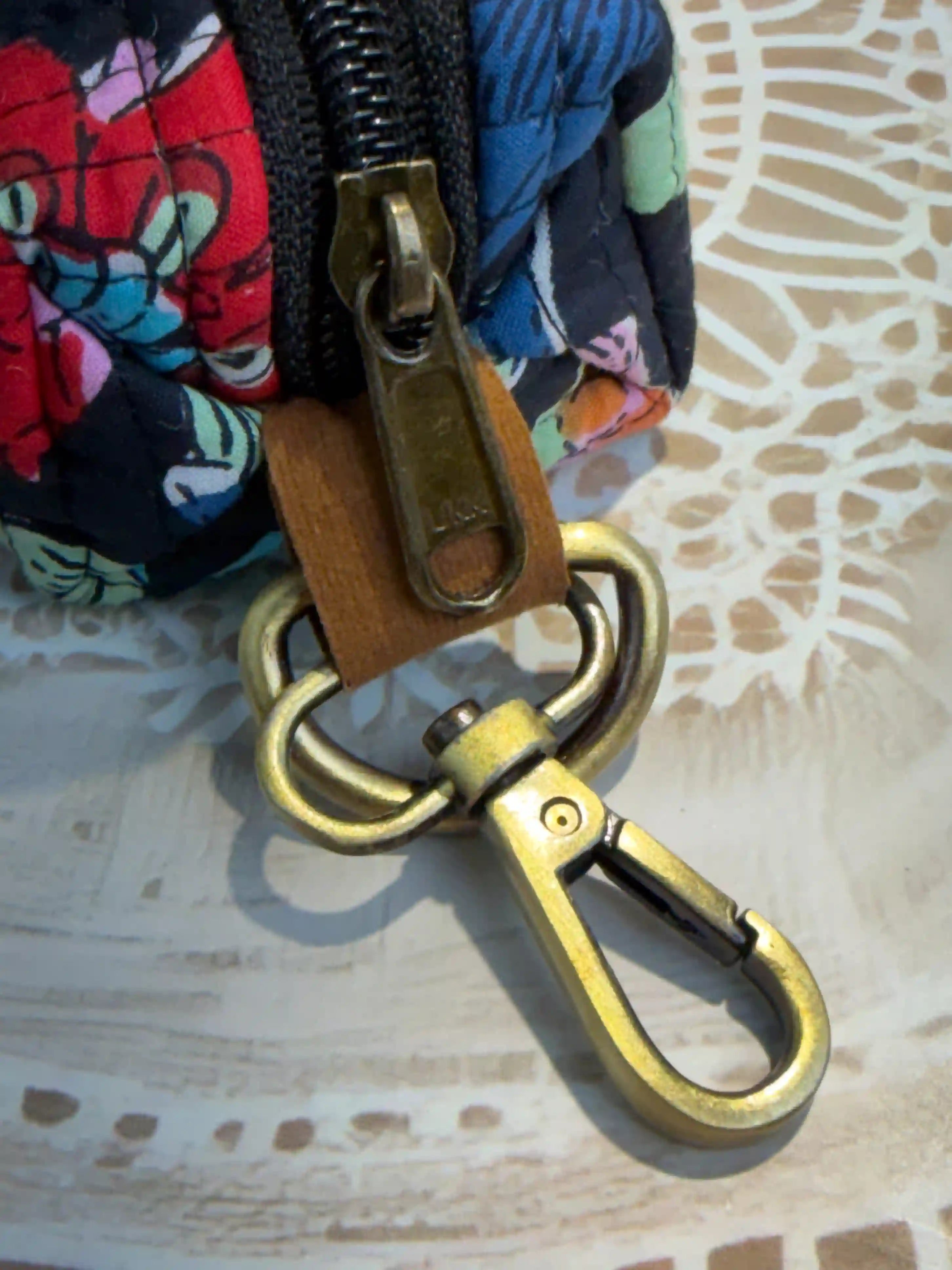 Hand block printed quilted cotton keychain pouch with multicolor floral design on black background, featuring red, yellow, and blue flowers with zip closure and metal keyring for coins and keys.