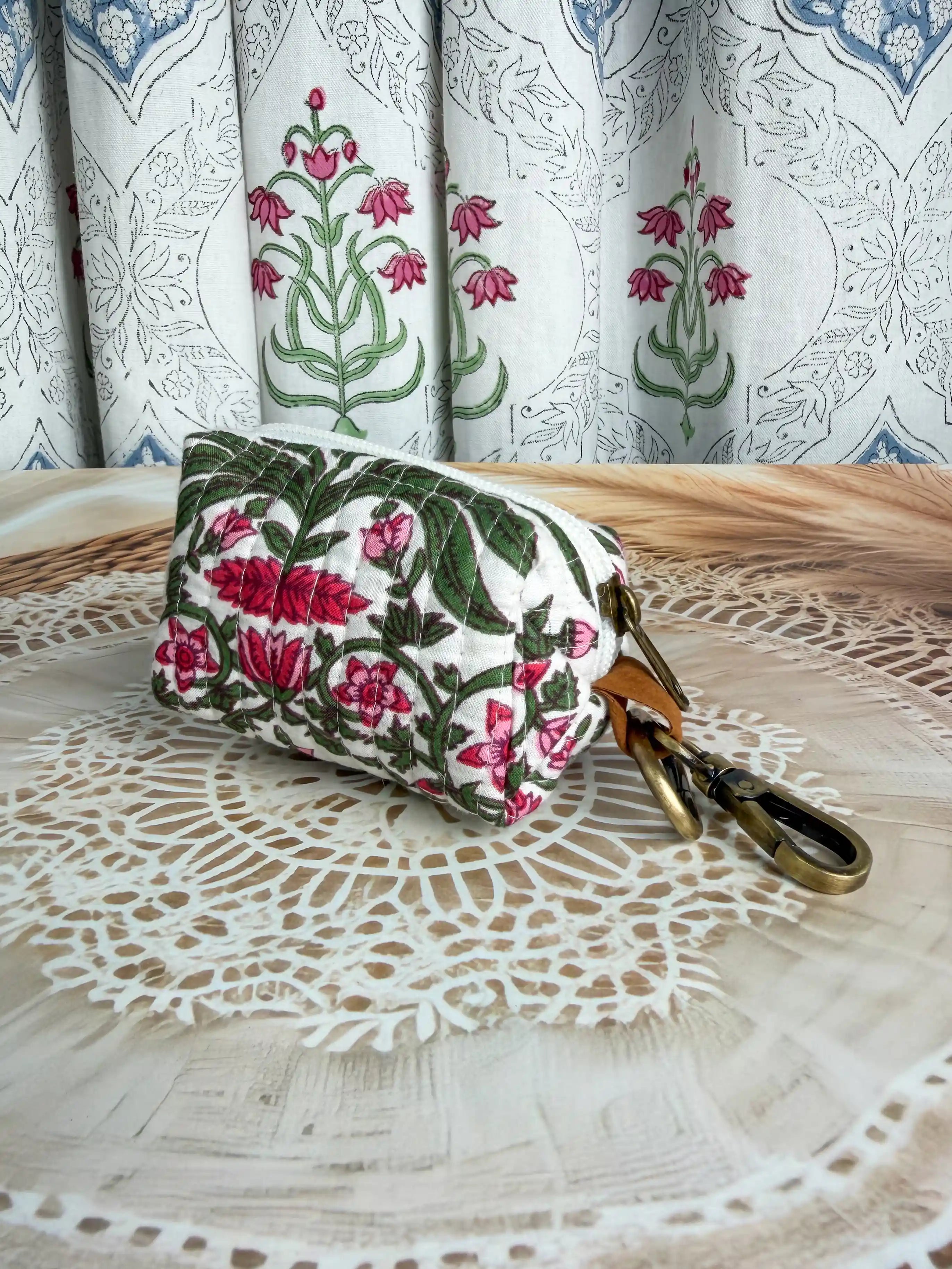 white quilted cotton keychain pouch with hand block printed red and green botanical floral design, durable zipper with metal keyring for carrying coins and essentials.