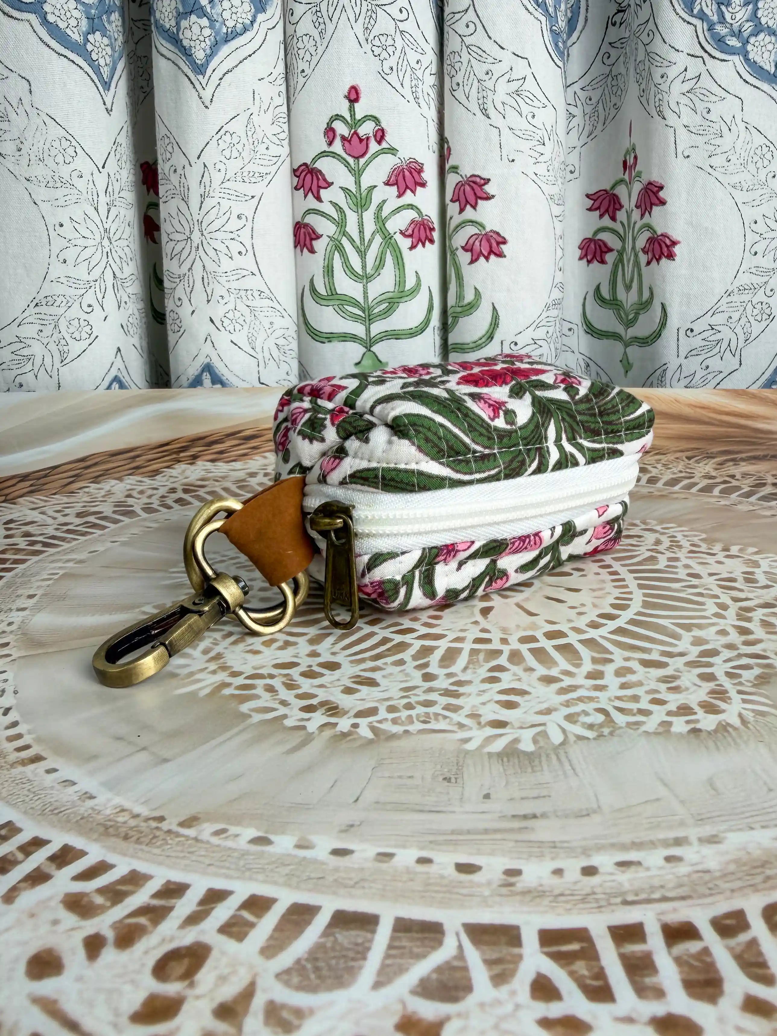 white quilted cotton keychain pouch with hand block printed red and green botanical floral design, durable zipper with metal keyring for carrying coins and essentials.
